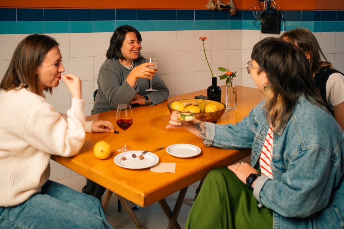 A group of women sitting around a table, one with a glass of wine